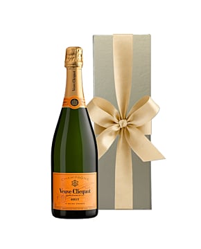 A bottle of Veuve Clicquot Yellow Label Brut Champagne standing next to an opulent gold luxury gift box finished with a large, hand-tied ribbon.